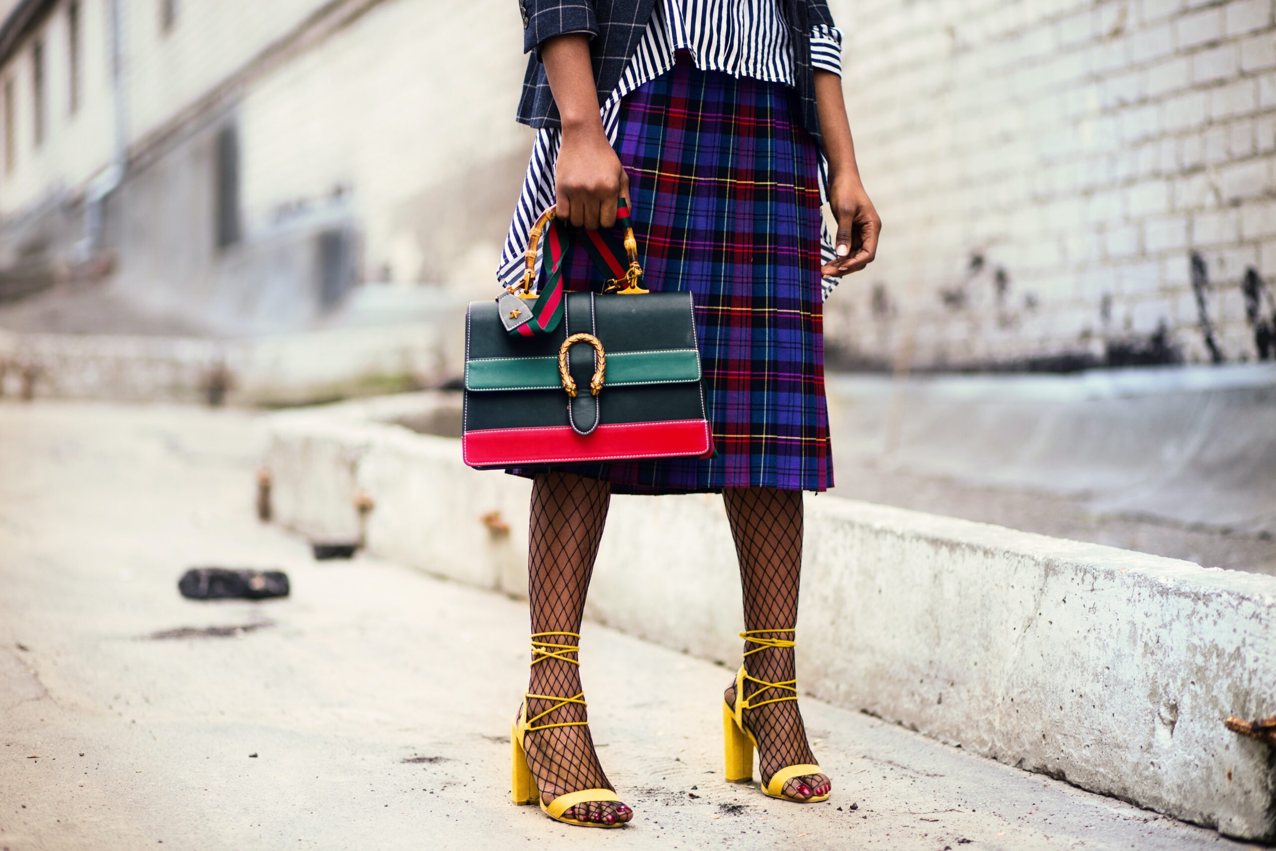a woman in a plaid skirt holding a multicolored purse.