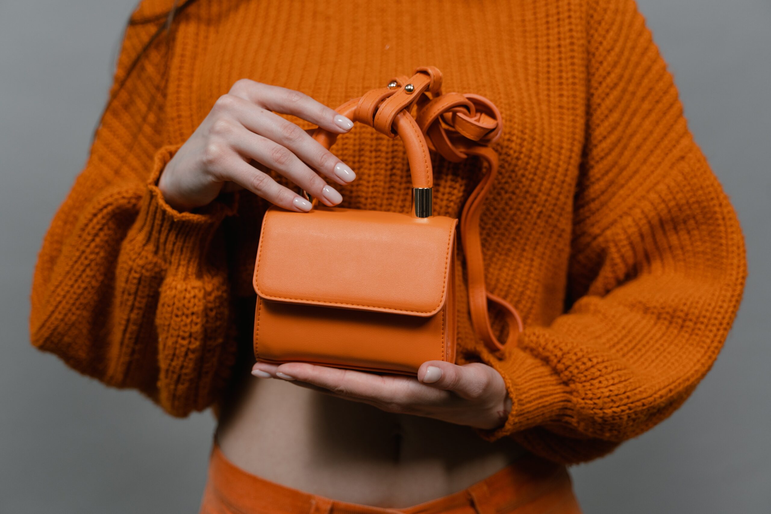 a woman holding an orange purse in her hands.