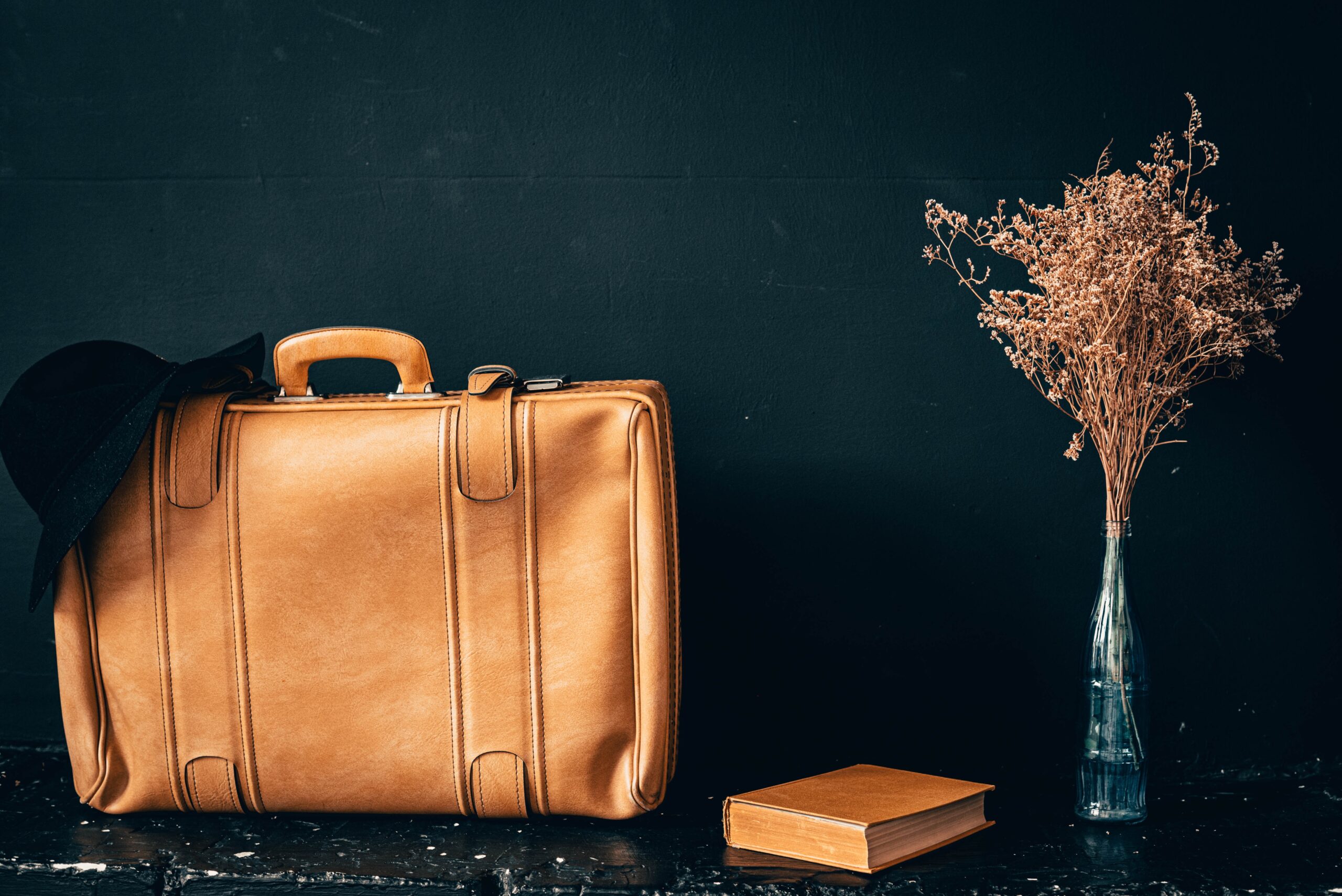 a brown leather suitcase sitting next to a vase of dried flowers.