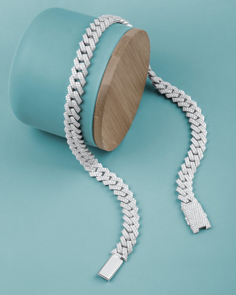 A silver thick iced chain and bangle on a blue background