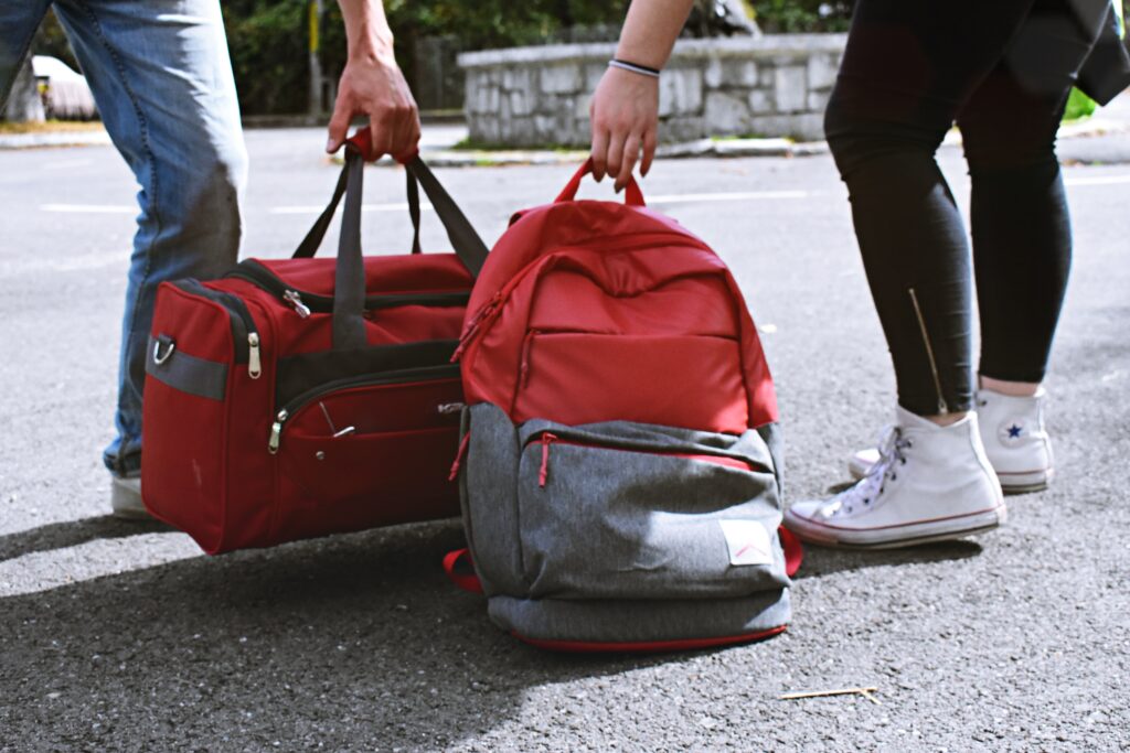 two people standing next to each other with luggage a duffel bag and backpack