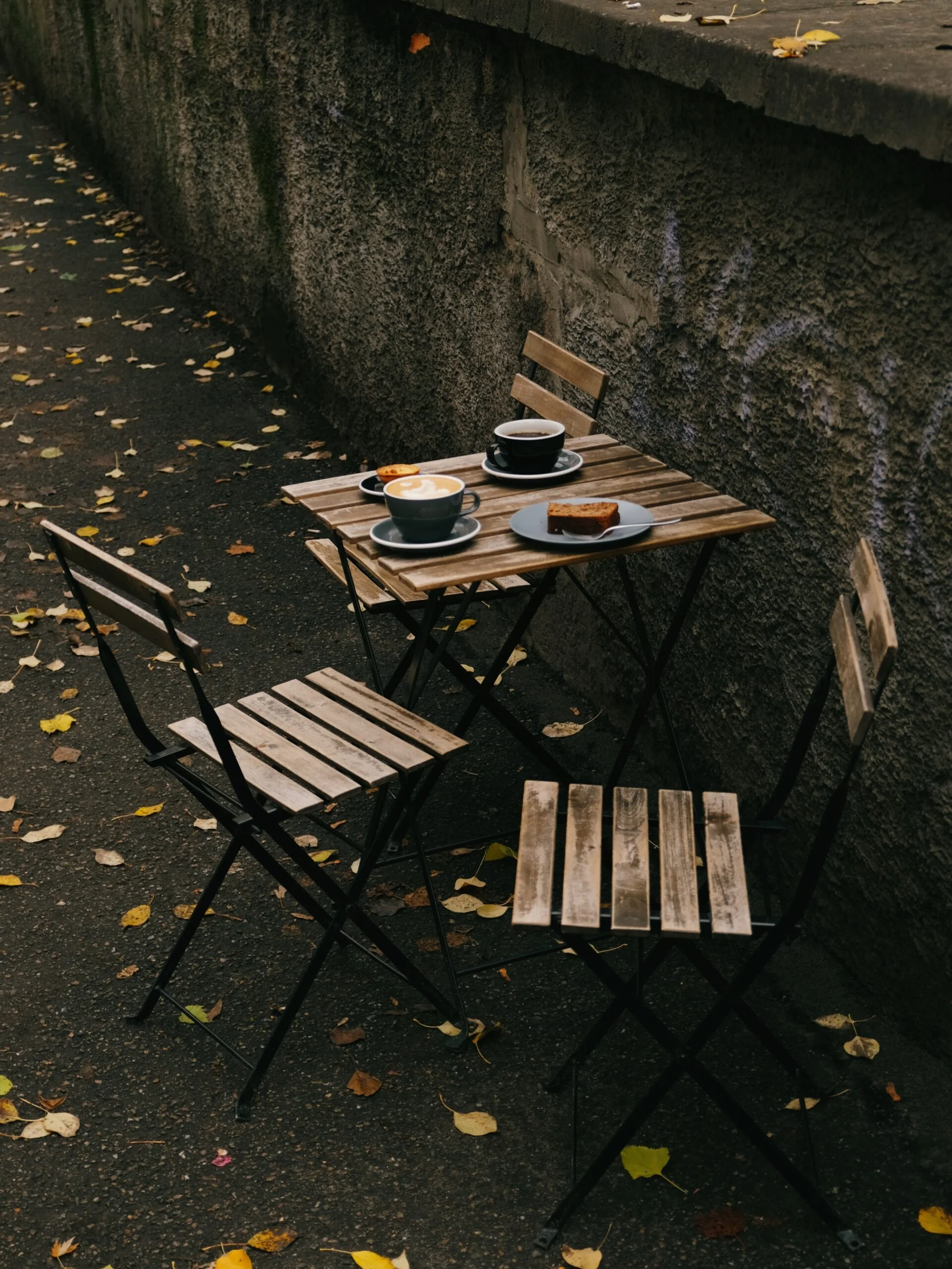 Modern table ware out in the sun placed on a wooden table with four chairs around it in the open